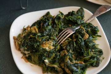 stir-fried kale with eggs on a white plate with fork