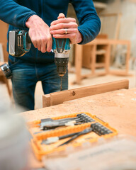 Close Up Of Carpenter At Workbench In Workshop Using Cordless Electric Drill