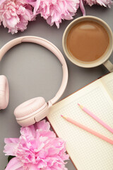 Modern pink headphones with flowers peonies and notebook on grey background. Vertical photo