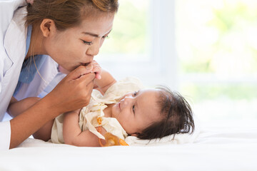 Happy family. Asian mother kissing her adorable Caucasian newborn 3 months old baby girl hands,...