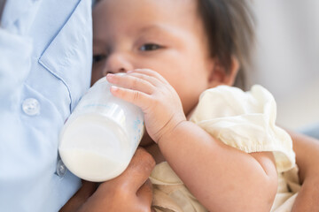 Cute Caucasian little newborn 3 months old baby girl drinking milk from bottle. Mother holding...