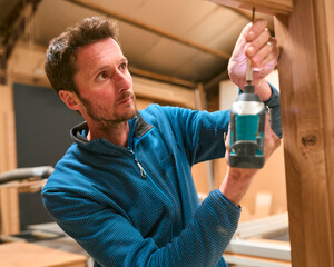 Carpenter In Workshop Using Drill To Attach Piece Of Wood To Window Frame