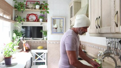A mature man over fifty years old, cleaning vegetables under the kitchen sink faucet, kitchen work. Daily life of people at home.