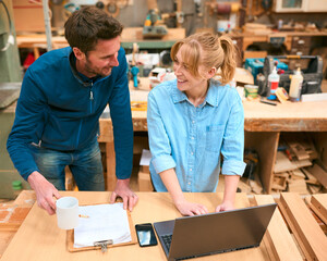 Male And Female Carpenters Working In Woodwork Workshop Using Laptop Together
