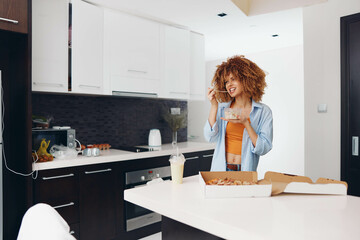 Woman holding pizza box in front of kitchen counter, preparing to enjoy a delicious meal at home