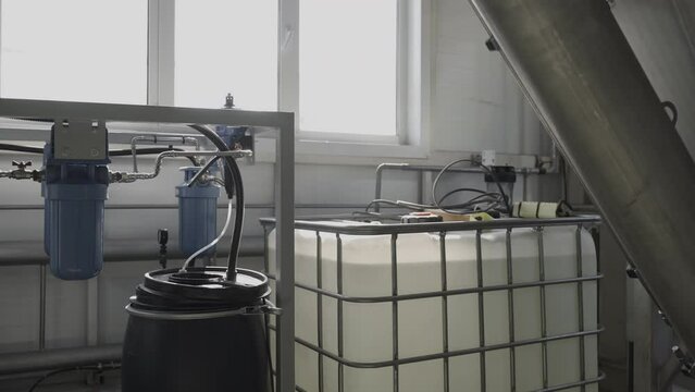 Bulk container with liquid in near workshop window. Modern equipment for materials processing in production shop. Industrial facility