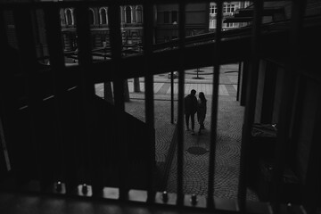 View through lattice to young couple standing on street, looking each other and holding hands.