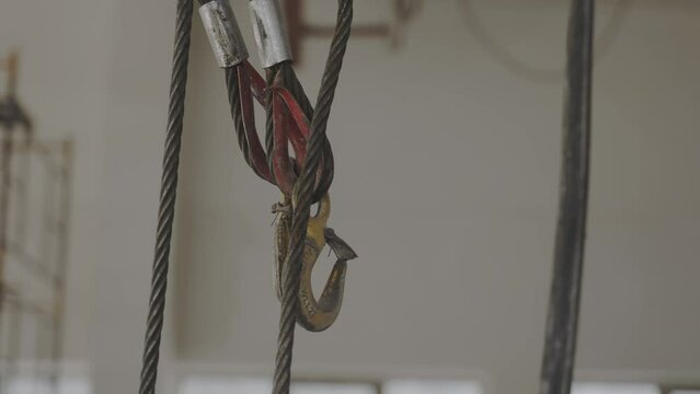 Metal rope with hooks for heavy cargo transportation in warehouse closeup. Crane hoist fastening hanging in industrial storage. Plant equipment