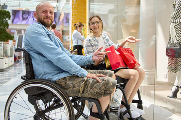 Smiling man in a wheelchair and woman with shopping bags enjoying time at the mall