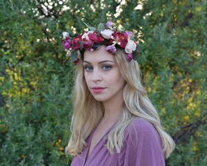 close up portrait of pretty blonde female model wearing a flower crown wreath and purple dress. ...