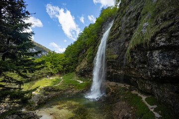 Obraz premium Fontanon of Goriuda, Udine. Wonderful waterfall that falls from a cliff. The force of the waterfall is a sight to behold. Hiking, trekking in the open area surrounded by woods. Summer holidays, peace.