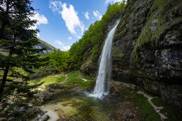 Fototapeta premium Fontanon of Goriuda, Udine. Wonderful waterfall that falls from a cliff. The force of the waterfall is a sight to behold. Hiking, trekking in the open area surrounded by woods. Summer holidays, peace.