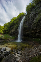 Fontanon of Goriuda, Udine. Wonderful waterfall that falls from a cliff. The force of the waterfall is a sight to behold. Hiking, trekking in the open area surrounded by woods. Summer holidays, peace.