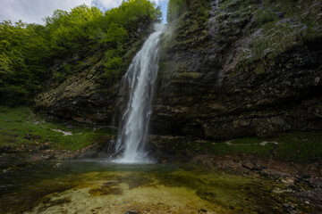 Fontanon of Goriuda, Udine. Wonderful waterfall that falls from a cliff. The force of the waterfall is a sight to behold. Hiking, trekking in the open area surrounded by woods. Summer holidays, peace.