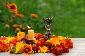 Triple Goddess figurine with candle and colorful flowers in garden, nature background. Symbol of...