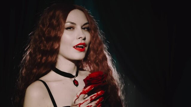 fantasy vampire woman licks drops of blood fingers hands, red lips evil beauty face pale skin sexy girl white teeth fangs. hand holding red rose flower. halloween holiday make-up Gothic lady art 4k