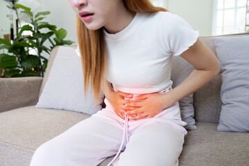 A woman is sitting on a couch with a stomach ache