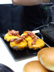 hamburguesas gourmet de carne, queso fundido y panceta haciéndose a la parrilla