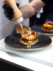 chef echando salsa a una hamburguesa con carne,  queso y beicon para servirla