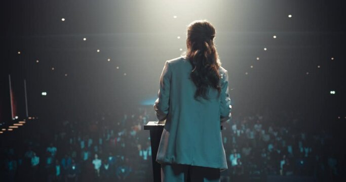 Businesswoman Walking Out on Stage to Give a Talk at a Global Finance Summit. Audience Listening to Her Insightful Talk. Speaker Standing with Her Back to Camera While Making a Motivational Speech