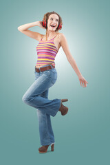 Joyful young woman who is listening to music through red headphones, dancing and looks to the side with her blue eyes while being isolated on a blue background