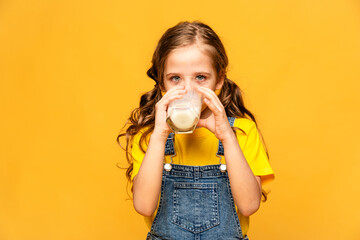 Happy smiling little girl drinking milk on a light yellow background, space for text, children...