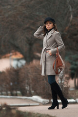 Fototapeta premium A girl on the street in a gray coat and a brown bag. Grain effect used