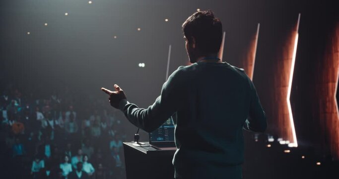 Indian Business Leader Giving a Talk on Stage at a Global Finance Summit. Audience Listening to an Insightful Talk. Speaker Standing with His Back to Camera While Making a Motivational Speech
