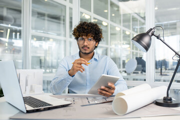 Architect working on a project in a modern office environment, using a digital tablet and architectural plans.