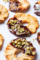 Dried pineapple chips with dark chocolate, pistachio and coconut on white background. Vegan dessert.