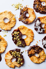 Dried pineapple chips with dark chocolate, pistachio and coconut on white background. Vegan dessert.