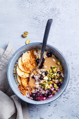 Overnight oatmeal with black currants, pistachios, coconut crumbs and peanut butter, gray background.