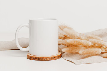 Mockup mug on wooden cup coaster on the table with linen cloth and bunny tail grass. Mockup mug for...