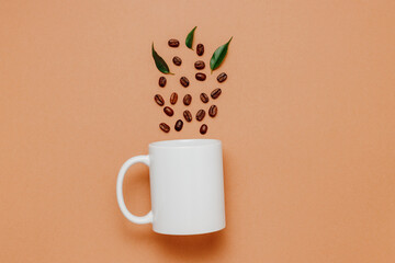 Mockup mug with coffee beans and green leaves on brown background, top view. White mockup coffee...
