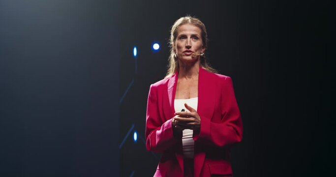 Beautiful Adult Female in a Red Suit Making a Passionate Lecture with a Big Screen Showing Different Analytical Data in the Background. Representative Sharing a Company Earning Report to Shareholders