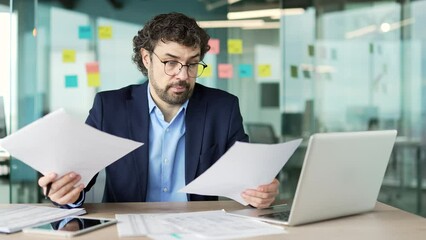 Confused puzzled businessman or worker having difficulty with paper work sitting at workplace in business office. Frustrated man financier in suit checks documents, unhappy with bad financial results