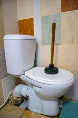 A serviceman is repairing a toilet with a hand plunger caused by a clogged toilet.