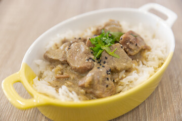 Baked pork rice with garlic sauce in a ceramic bowl on a wooden table in a restaurant.