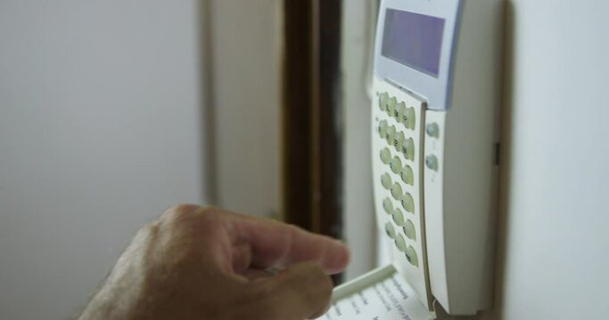 A mans hand is captured as he sets an alarm on a wall-mounted security keypad inside a house, ensuring safety and security.