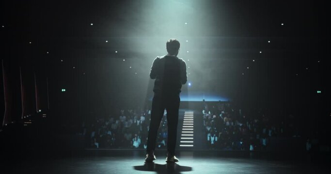 Young Thought Leader Standing on Stage, Making an Inspiring Presentation at Technology Conference. Indian Man Holding a Piece of Paper with Notes, Talking to an Audience in a Dark Venue