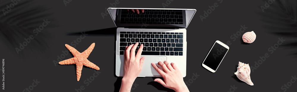 Poster person using a laptop computer with shells and starfish - flat lay
