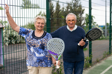 Portrait of sporty fit senior woman playing padel on open court on summer day, ready to hit ball....