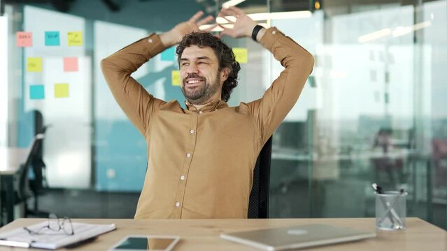 Satisfied businessman finished work on computer while sitting at desk at workplace in business office. Happy worker closes the laptop, stretches in chair, throwing his hands behind his head. Work done