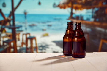 Two beer bottles standing on wooden table with beautiful ocean view, beach with resting zone, cafes...