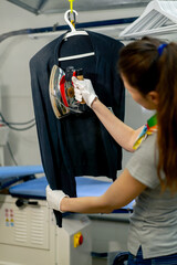professional dry cleaning young girl irons a black sweater on hanger with steam