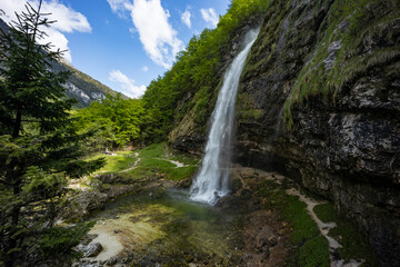 Fontanon of Goriuda, Udine. Wonderful waterfall that falls from a cliff. The force of the waterfall is a sight to behold. Hiking, trekking in the open area surrounded by woods. Summer holidays, peace.