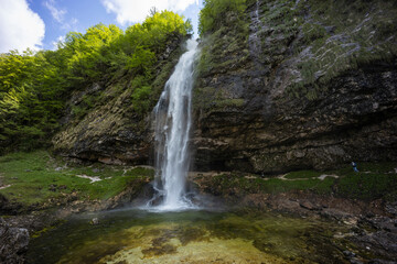 Fototapeta premium Fontanon of Goriuda, Udine. Wonderful waterfall that falls from a cliff. The force of the waterfall is a sight to behold. Hiking, trekking in the open area surrounded by woods. Summer holidays, peace.