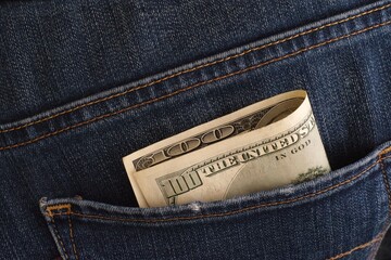 A close-up shot of a one hundred dollar banknote in the back pocket of blue jeans