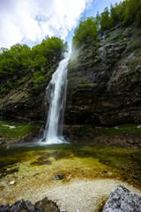 Fontanon of Goriuda, Udine. Wonderful waterfall that falls from a cliff. The force of the waterfall is a sight to behold. Hiking, trekking in the open area surrounded by woods. Summer holidays, peace.