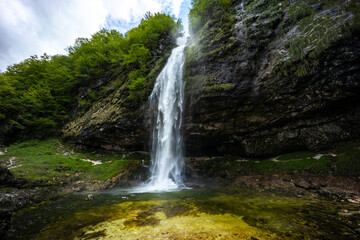 Fototapeta premium Fontanon of Goriuda, Udine. Wonderful waterfall that falls from a cliff. The force of the waterfall is a sight to behold. Hiking, trekking in the open area surrounded by woods. Summer holidays, peace.